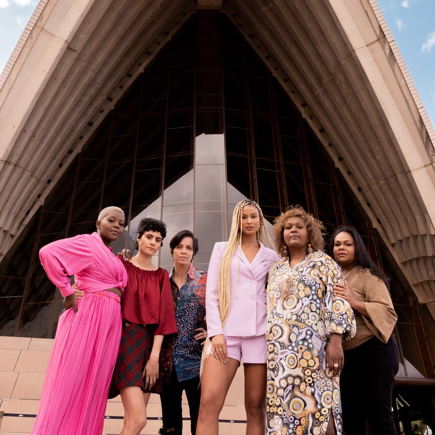 Six artists standing in front of the Sydney Opera House dressed formally