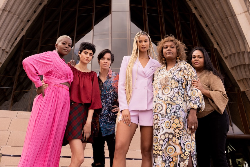 Six artists standing in front of the Sydney Opera House dressed formally