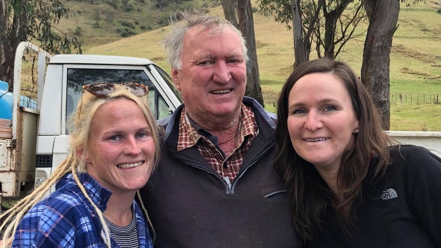 Two women stand of either side of a man on a farm 