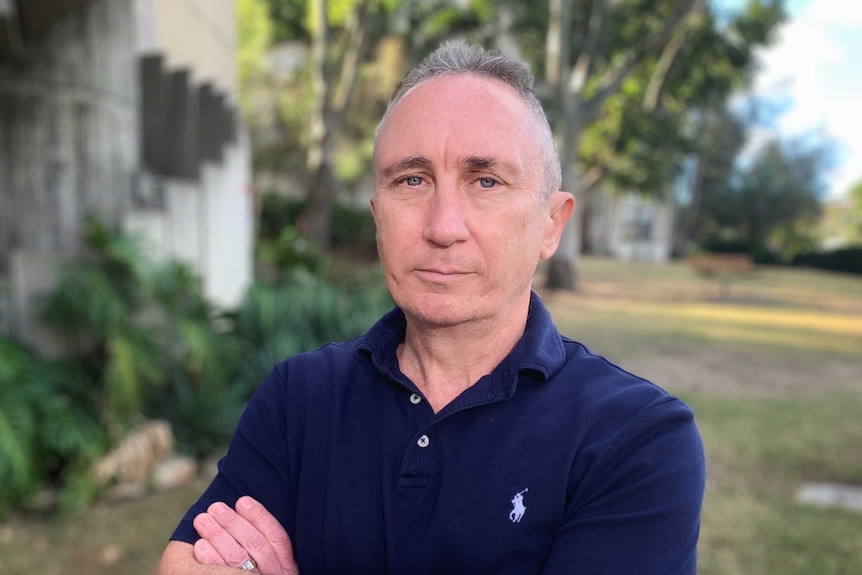 Mr Dodrill wears a blue polo shirt, arms crossed, posing for camera in a garden.