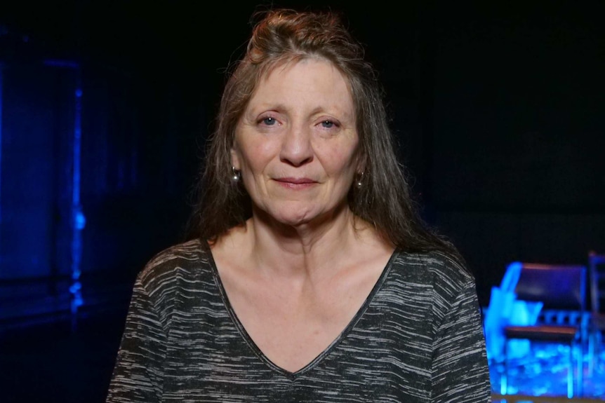 Susan McDonald-Timms poses for a portrait photograph in front of a blue-lit stage.