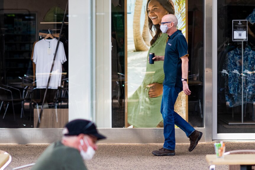 A man wearing a face mask walks in front of a shop window in the Smith St Mall in Darwin's CBD.