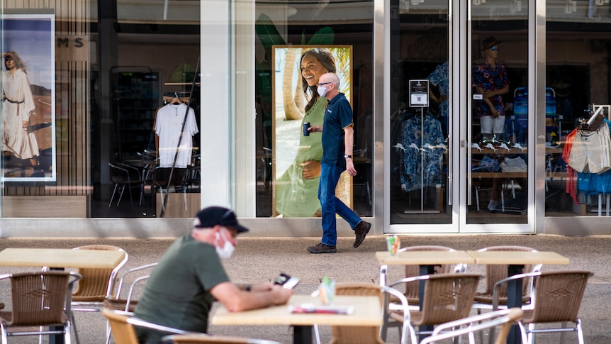 A man wearing a face mask walks in front of a shop window in the Smith St Mall in Darwin's CBD.