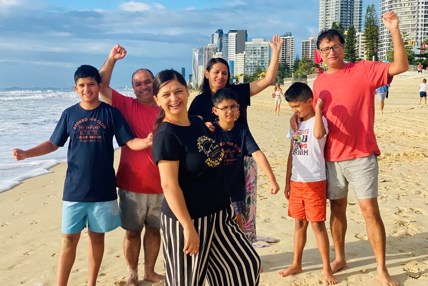Four adults and three children standing and smiling on Surfers Paradise beach with buildings in background.  