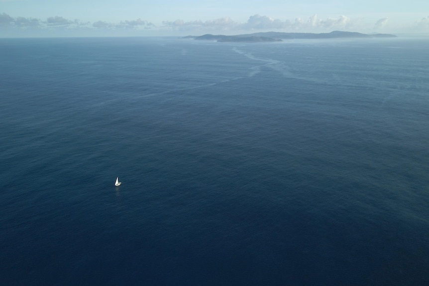 an aerial shot of the sail boat as a tiny speck in the wide open ocean