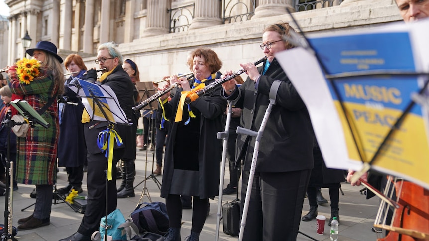 Musicians dressed in black clothes with blue and yellow scarves and ribbons, playing in support of the Ukrainian people.
