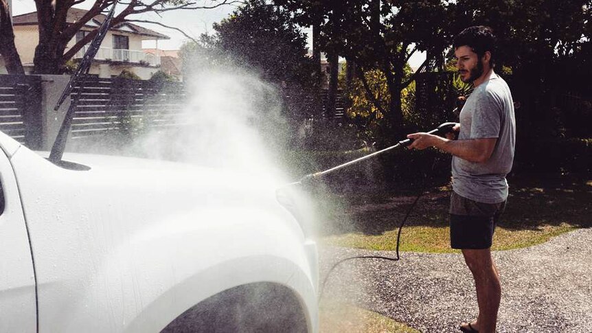 A man washes his car in the driveway.