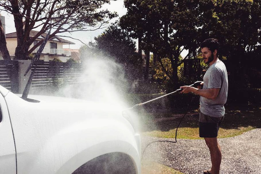 A man washes his car in the driveway.