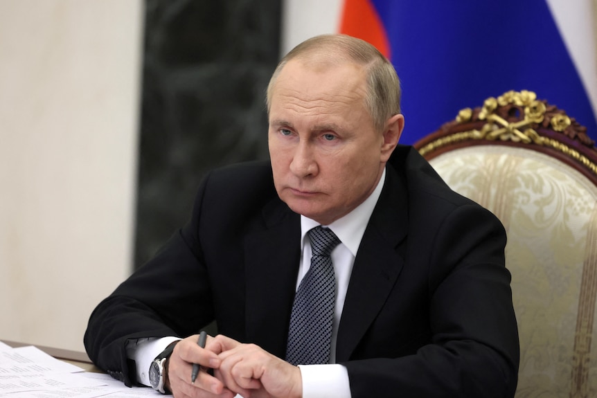 Russian President Vladimir Putin sit at a desk intently.