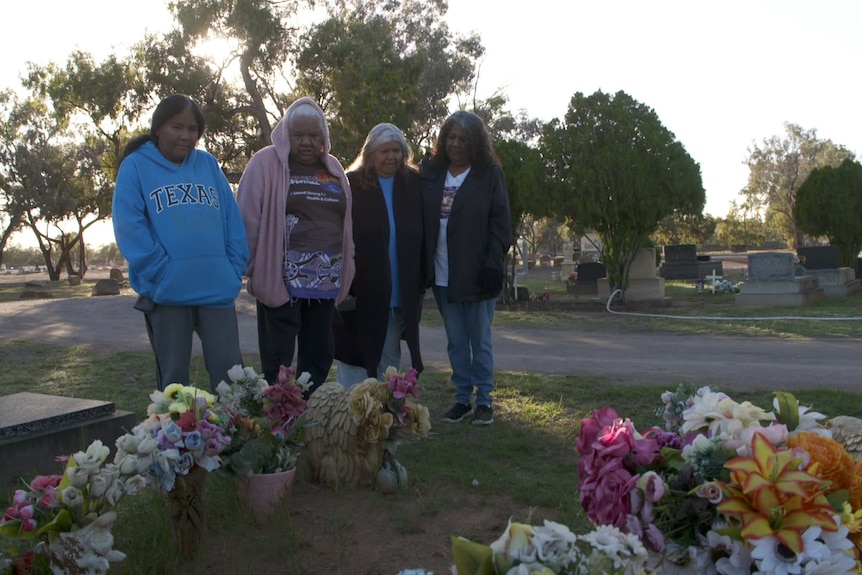 Four women stand in front of two graves.