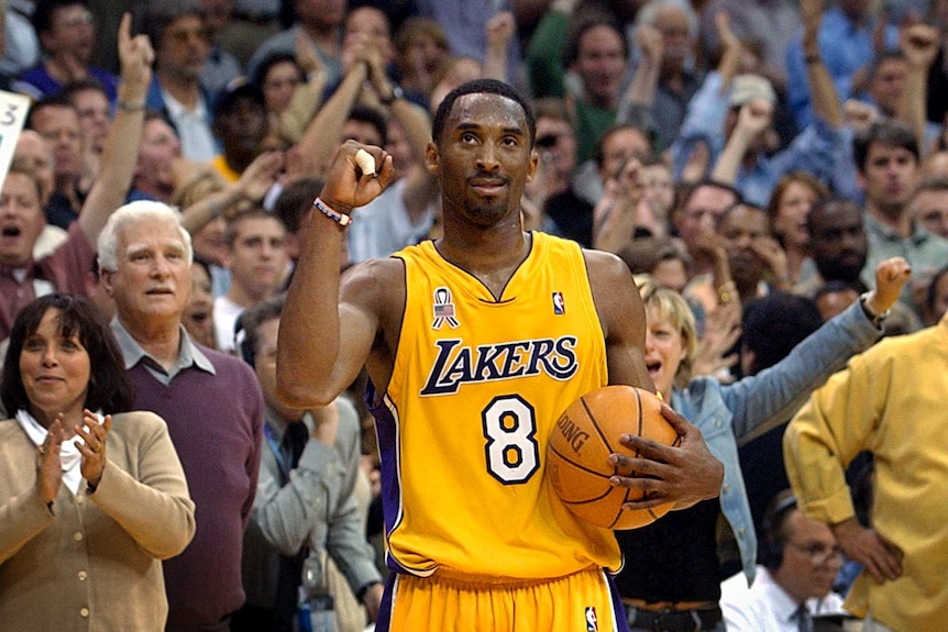 Kobe Bryant clenches his right fist and smiles, holding a basketball in his left hand