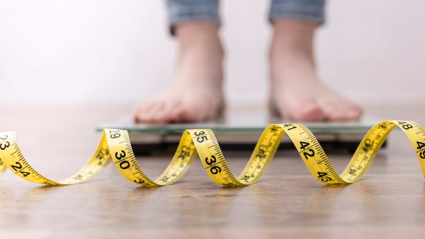 Female legs stepping on weigh scales with measuring tape
