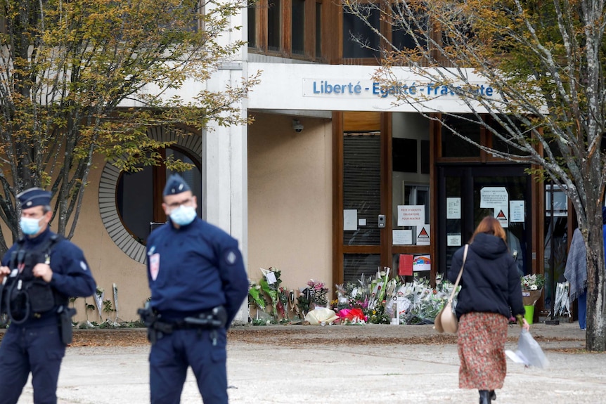 Police stand by as people bring flowers to the Bois d'Aulne college after the attack.