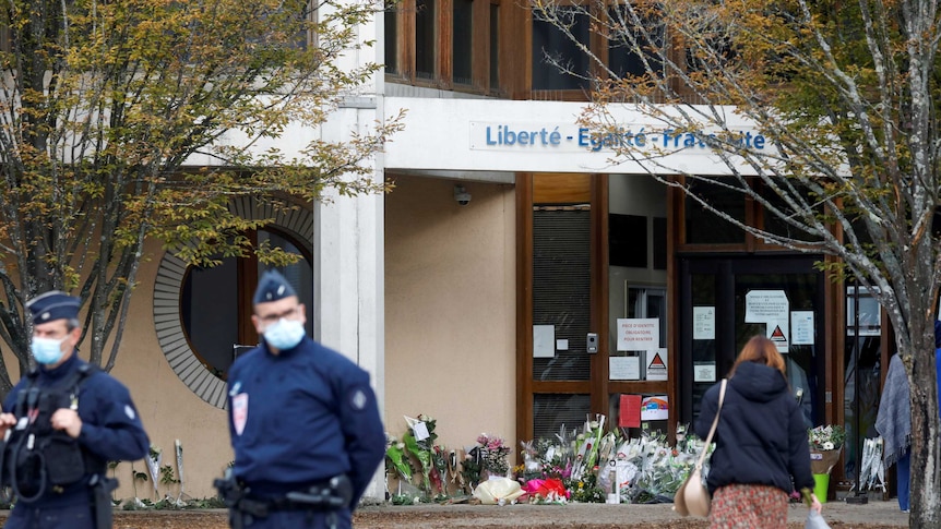 Police stand by as people bring flowers to the Bois d'Aulne college after the attack.