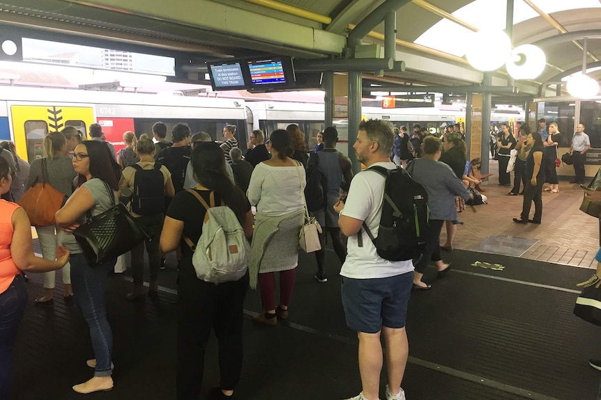 Commuters wait on platform with delayed train at Roma Street Station in Brisbane during severe storms.