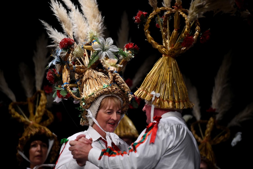 Two people wearing elaborate wicker hats hold hands as they participate in a dance