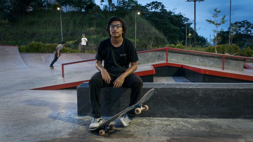 Aldy Agustiano sits on a platform in a Jakarta skatepark. He is lifting his skateboard with his foot.
