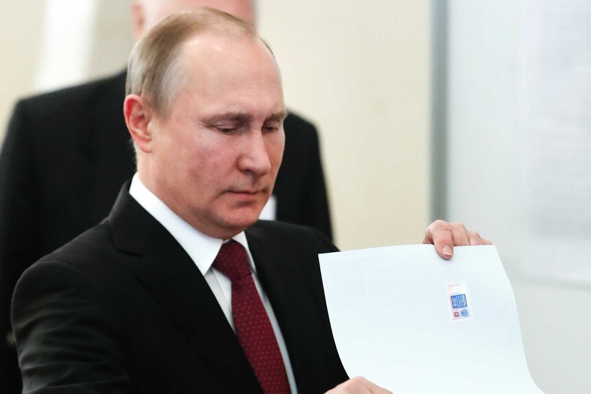 Medium shot of Vladimir Putin putting a large sheet of paper into a box.