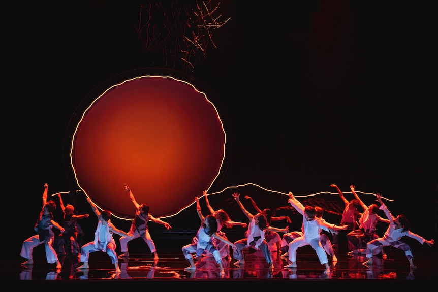 A group of dancers on stage, with a giant round sun-like ball projected behind them.