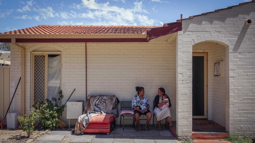 Two women sit out the front of a brick home in suburban Perth.