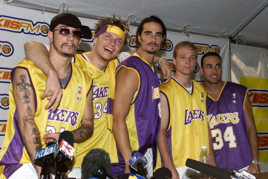 The Backstreet Boys pose as a group in Lakers basketball jerseys. 