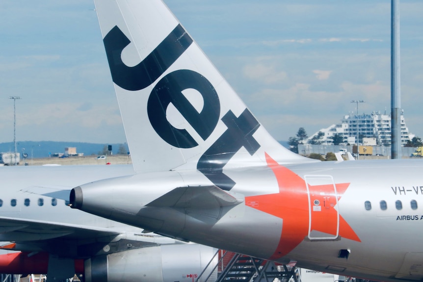 A close up of a Jetstar plane's branded tail parked at an airport.