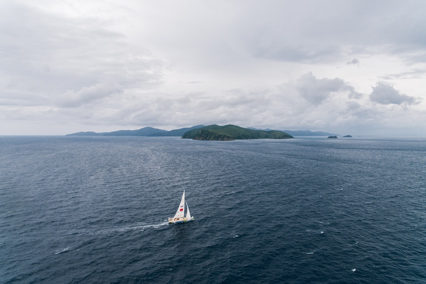 A birds eye view of a yacht in the middle of the ocean on a cloudy day. 