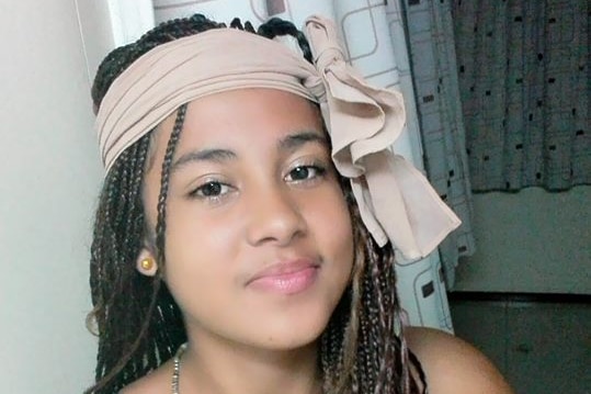 A young woman with long braided hair and a beige scarf wrapped around her head