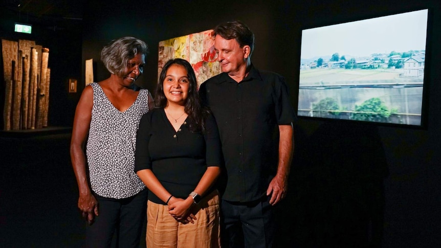 A photo of 18-year-old Siena Stubbs standing with her mother and father in the Museum and Art Gallery of the NT.