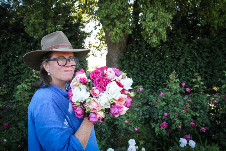 A woman wearing blue, holds a vibrant bouquet of fragrant garden roses.