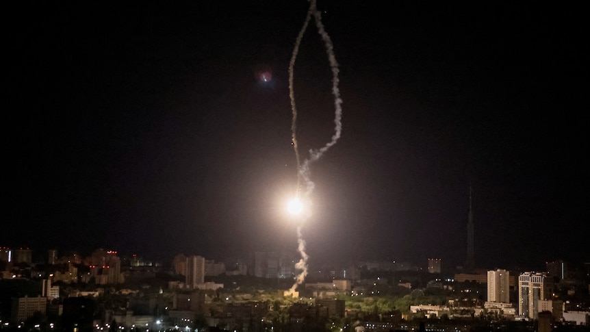 A missile is shot down over Kyiv, leaving a ball of light and a vertical trial of smoke in dark night sky. 