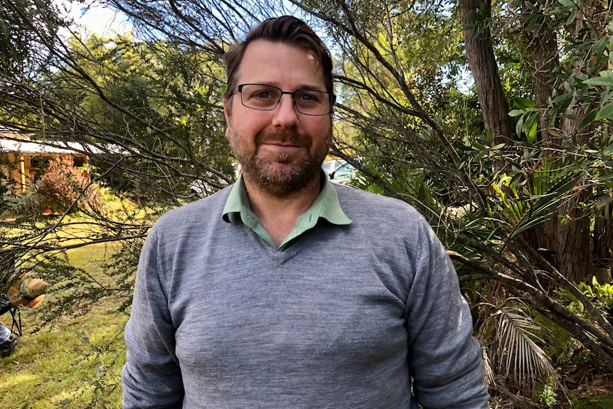 A man wearing glasses and a jumper looks at the camera.