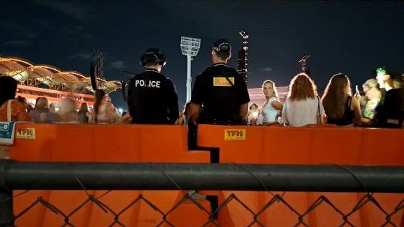A low cyclone fence, orange emergency barrier and the back of two police officers