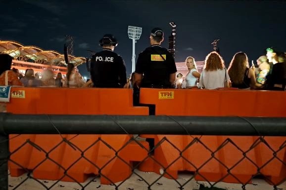 A low cyclone fence, orange emergency barrier and the back of two police officers