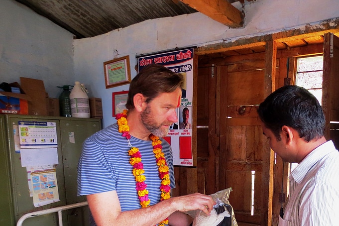 A man wearing a flower lei shows a packet containing some equipment to another man