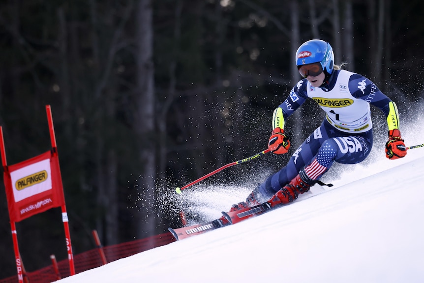 A skiier leans into a corner and tries to control her turn as a spray of snow shavings fly in the air.