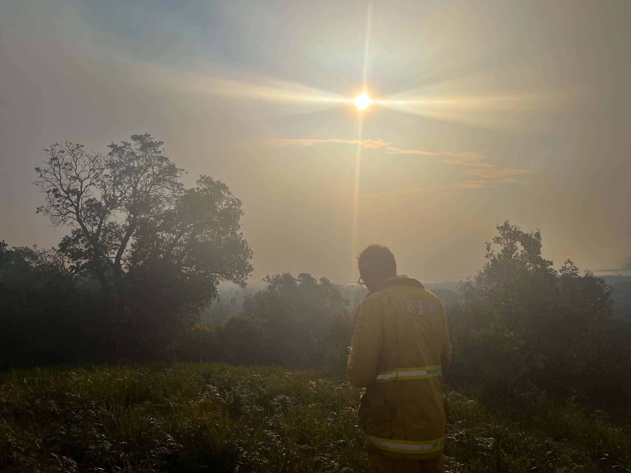 A firefighter stands amid a haze of smoke as the sun shines through.