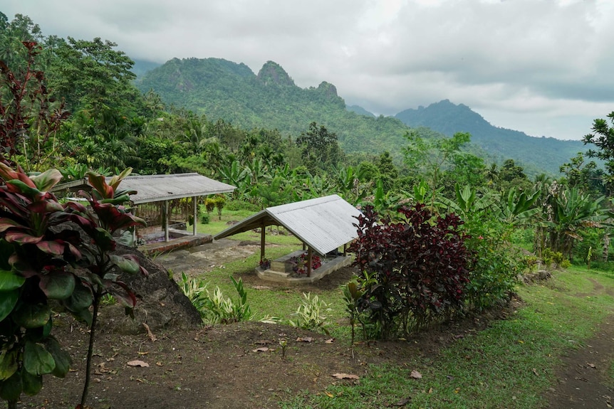 Two graves with roofs sit atop a hillside with mountains in the background.