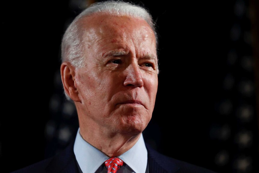 US presidential candidate Joe Biden, wearing a dark suit and red tie, frowns and looks off into the distance