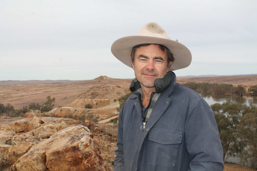 a man smiles in the middle of a desert while he wears an Akubra