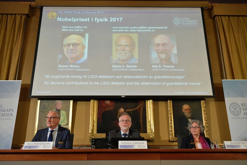 Three panellists sit in a row with the names and faces of the winners projected onto a screen behind them.