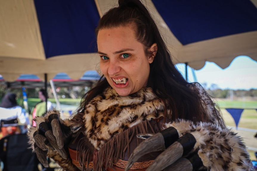 A woman dressed in a monster costume bares her teeth to reveal fake fangs. 