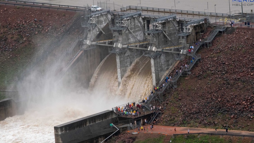 Crowd of people watching water rushing out a gate dam