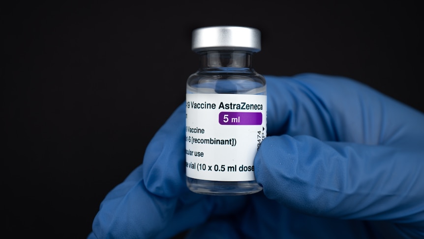 A person with a blue medical glove holds up a vial of AstraZeneca vaccine.