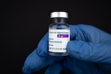 A person with a blue medical glove holds up a vial of AstraZeneca vaccine.