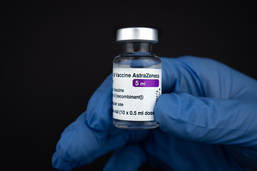 A person with a blue medical glove holds up a vial of AstraZeneca vaccine.