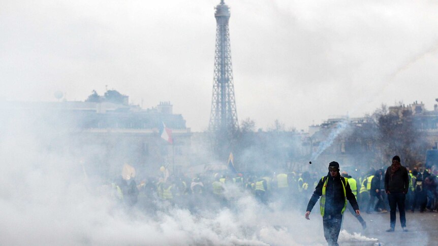 Gilets Jaunes protesters walk through tear gas smoke on Champs Elysees with Eiffel Tower in background