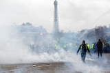 Gilets Jaunes protesters walk through tear gas smoke on Champs Elysees with Eiffel Tower in background