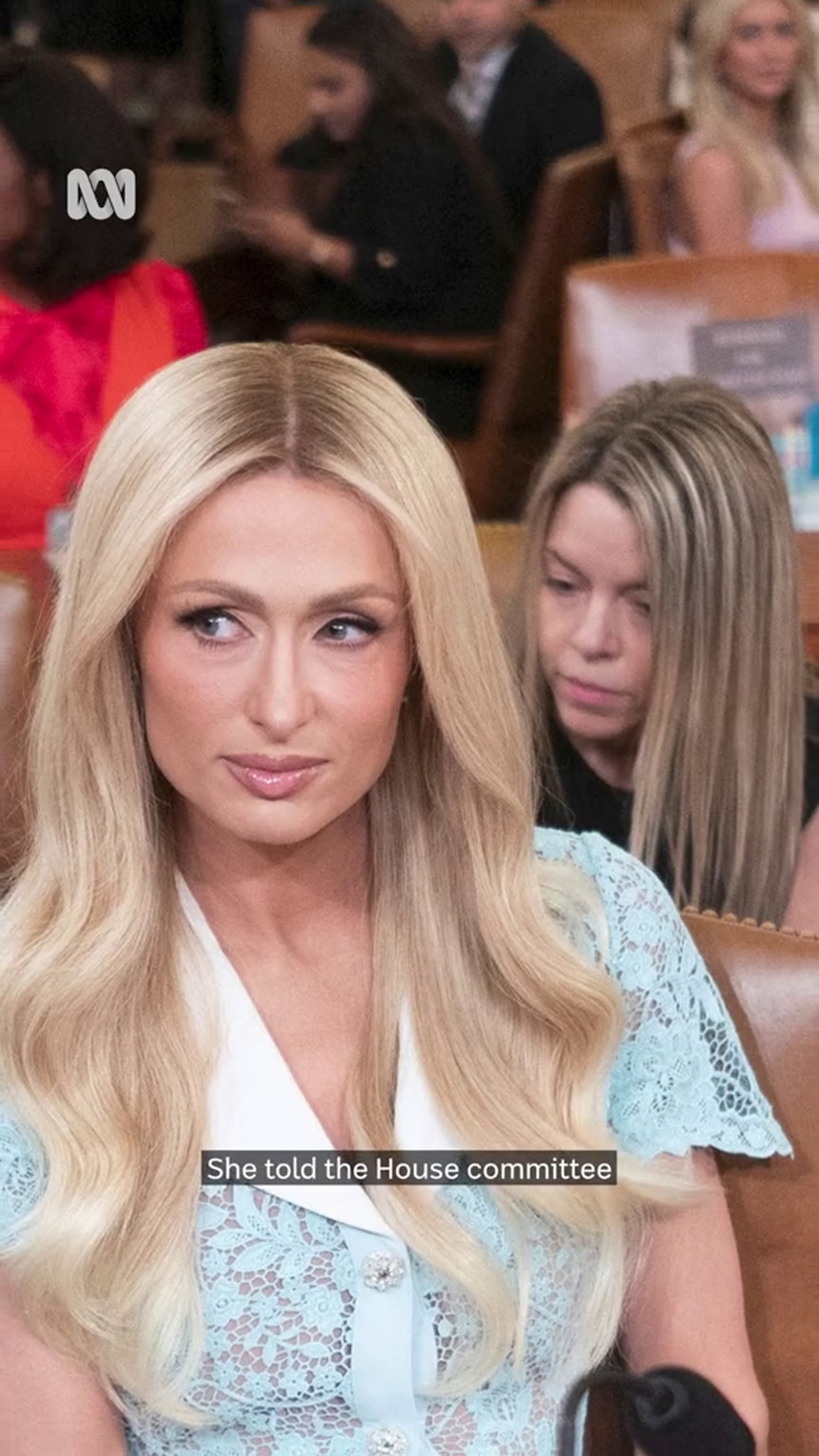 Paris Hilton looks off screen with with people sitting around tables in the background
