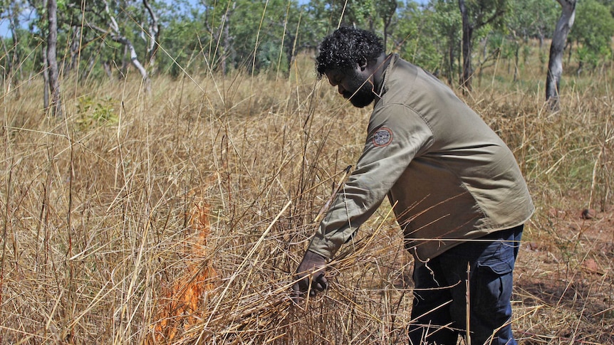 a man lighting a fire in dry grass